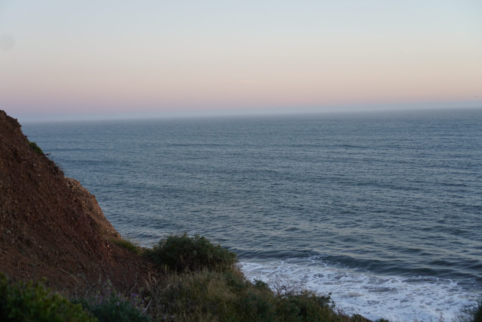 Pink dusk over the ocean from a coastal bluff.